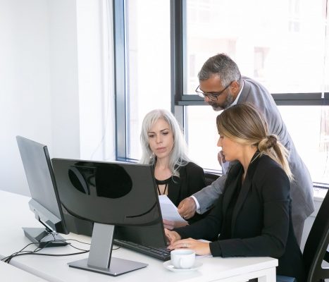 serious-business-group-three-analyzing-reports-sitting-workplace-with-monitors-together-holding-reviewing-discussing-papers-copy-space-business-meeting-concept-min